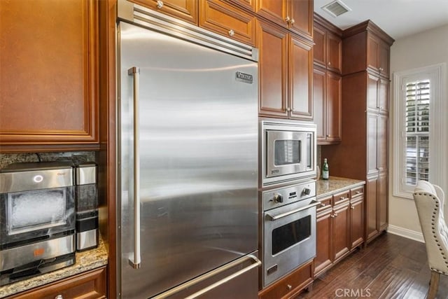 kitchen with built in appliances, dark hardwood / wood-style flooring, and light stone countertops