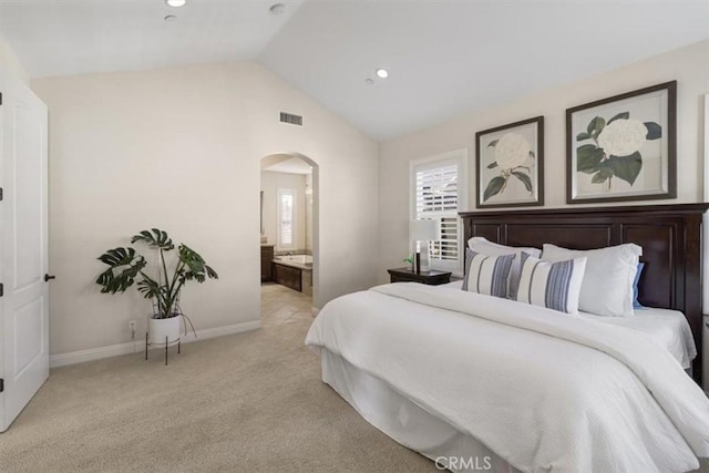 bedroom with light carpet, connected bathroom, and vaulted ceiling