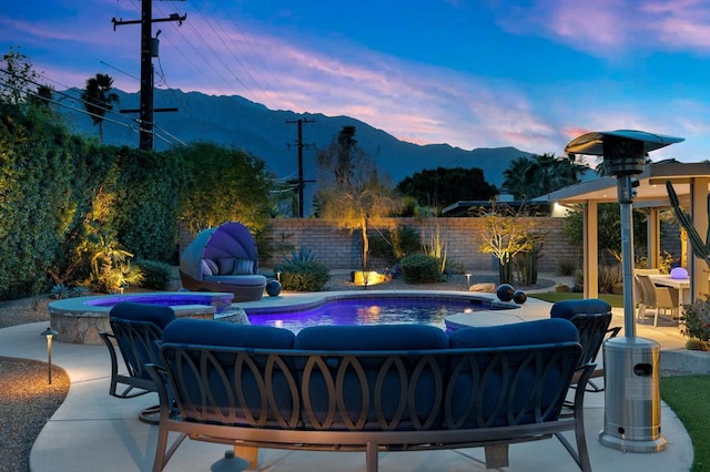 pool at dusk featuring a mountain view, a patio area, an outdoor living space, and an in ground hot tub