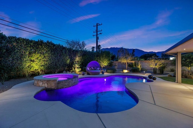 pool at dusk with an in ground hot tub, a mountain view, and a patio