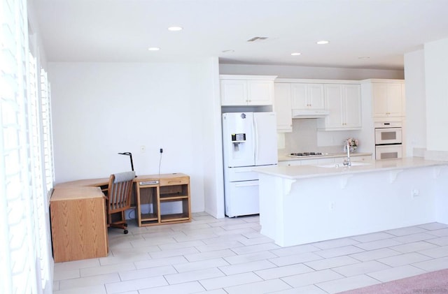 kitchen featuring a breakfast bar area, white cabinetry, sink, and white appliances