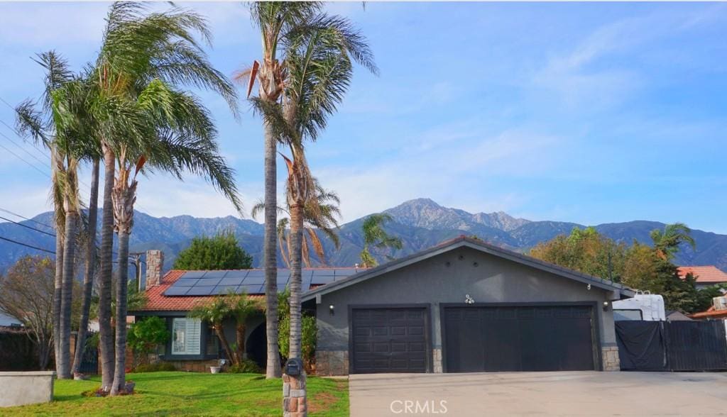 ranch-style house with stucco siding, a mountain view, a front yard, a garage, and solar panels