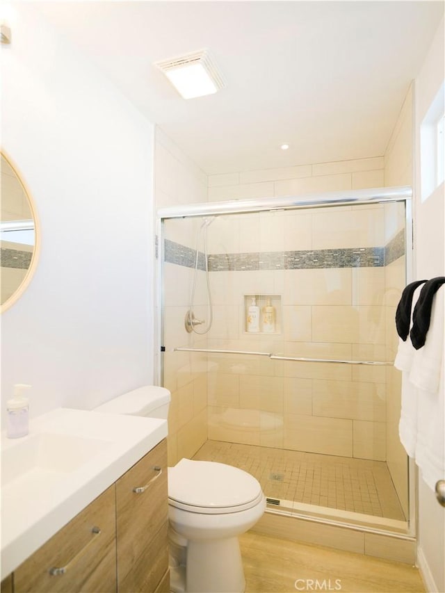 bathroom featuring wood-type flooring, vanity, toilet, and a shower with door