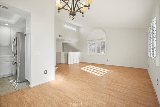 unfurnished living room with an inviting chandelier, lofted ceiling, and light hardwood / wood-style flooring