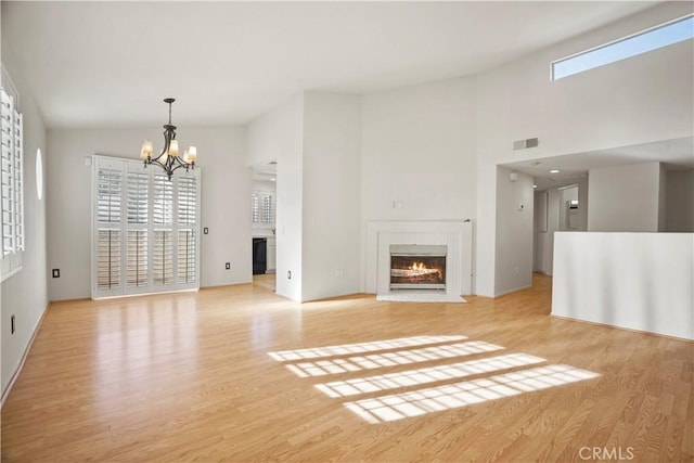 unfurnished living room featuring a notable chandelier, light wood-type flooring, and high vaulted ceiling