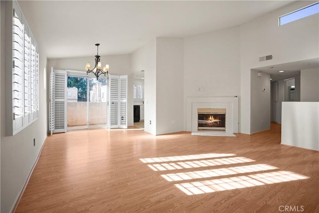 unfurnished living room featuring light hardwood / wood-style flooring, high vaulted ceiling, and a notable chandelier