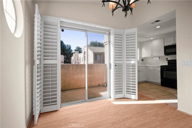 doorway to outside with vaulted ceiling, light hardwood / wood-style flooring, and a notable chandelier