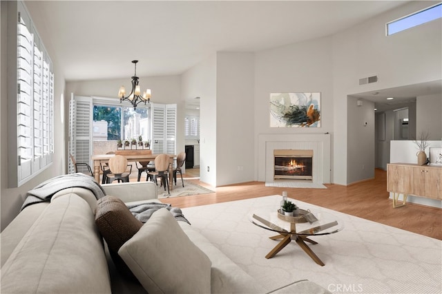 living room featuring high vaulted ceiling, an inviting chandelier, and light hardwood / wood-style flooring