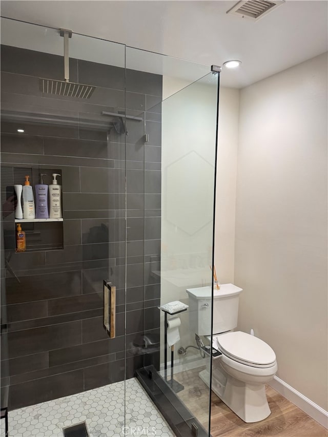 bathroom with hardwood / wood-style floors, toilet, and a shower with door