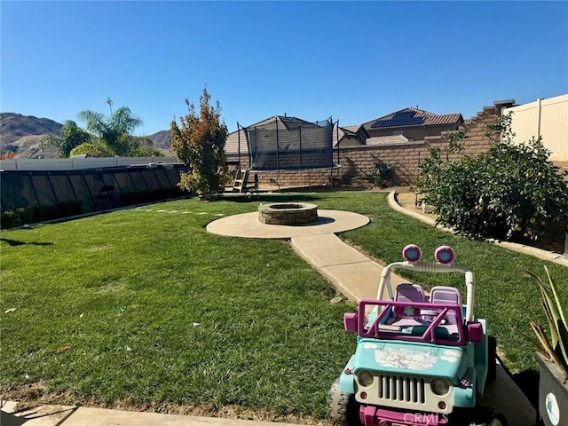 view of yard featuring a mountain view, a trampoline, a fire pit, and a patio area