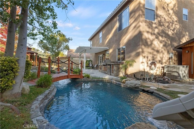 view of swimming pool featuring a pergola, a wooden deck, a patio, and an outdoor kitchen