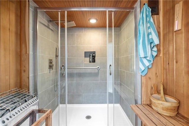 bathroom featuring a shower with shower door, wooden walls, and wood ceiling