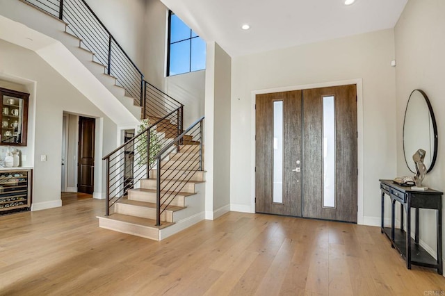 entrance foyer with wine cooler, a towering ceiling, and light wood-type flooring