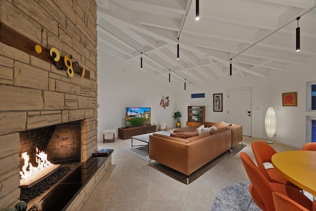 tiled living room featuring track lighting, beam ceiling, and a stone fireplace