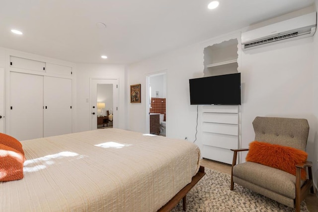 bedroom with ensuite bathroom, an AC wall unit, a closet, and hardwood / wood-style flooring