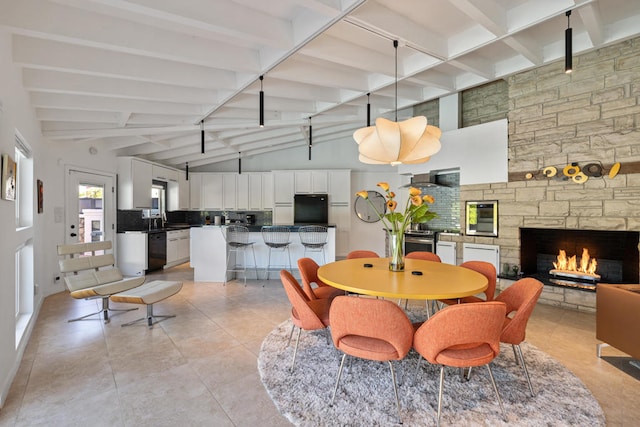 dining area with light tile patterned flooring, vaulted ceiling with beams, and a stone fireplace