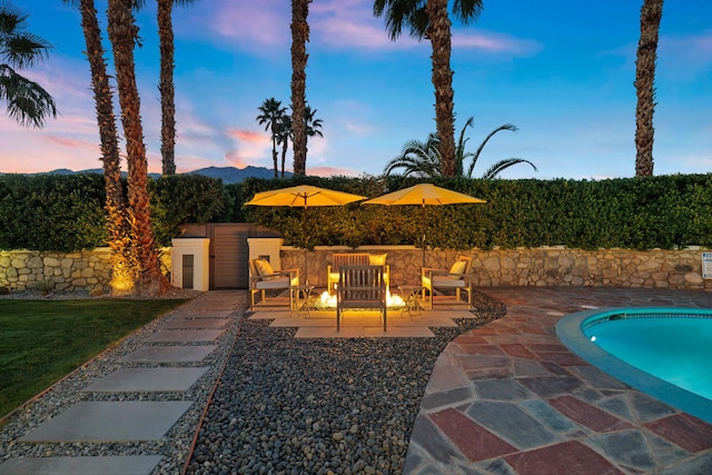 patio terrace at dusk featuring a fenced in pool and a fire pit