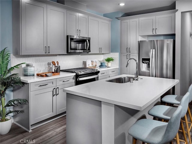 kitchen with sink, dark hardwood / wood-style floors, a breakfast bar area, a center island with sink, and appliances with stainless steel finishes