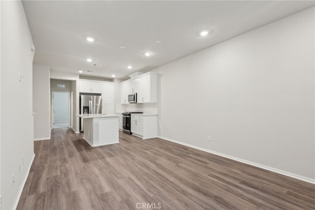 kitchen with stainless steel appliances, light countertops, open floor plan, white cabinets, and a kitchen island