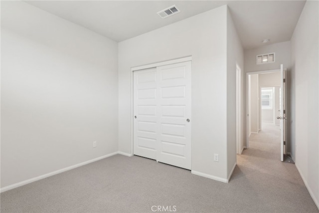 unfurnished bedroom with light carpet, baseboards, visible vents, and a closet