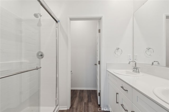 full bath featuring double vanity, a sink, a shower stall, and wood finished floors