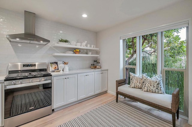 kitchen with stainless steel gas range, tasteful backsplash, light wood-type flooring, wall chimney range hood, and white cabinets