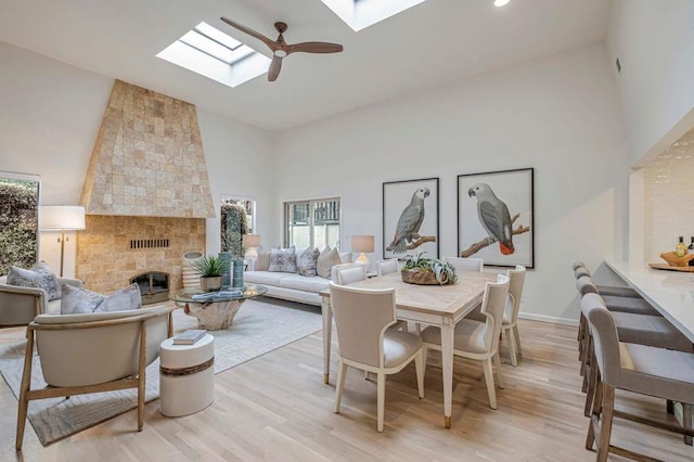 dining area with high vaulted ceiling, a fireplace, a skylight, ceiling fan, and light wood-type flooring