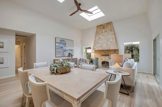 dining area with a skylight, high vaulted ceiling, a large fireplace, and light wood-type flooring