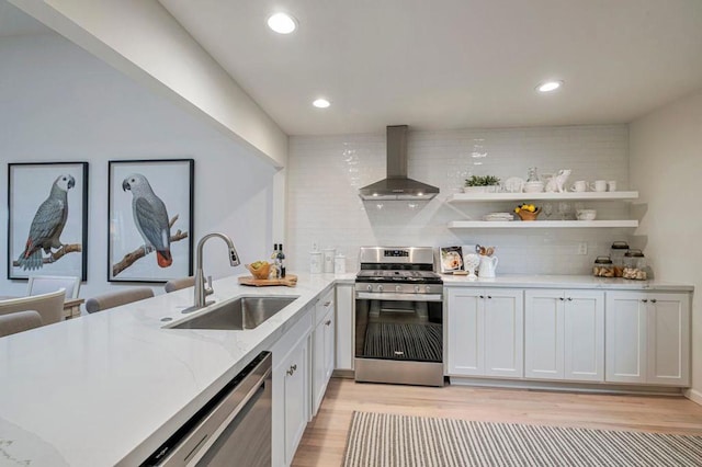 kitchen with wall chimney range hood, sink, white cabinetry, stainless steel appliances, and light stone counters