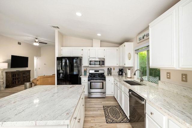 kitchen with white cabinets, sink, vaulted ceiling, light stone counters, and stainless steel appliances