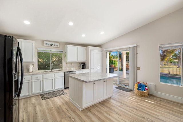 kitchen with black refrigerator, light wood-type flooring, stainless steel dishwasher, a kitchen island, and white cabinetry