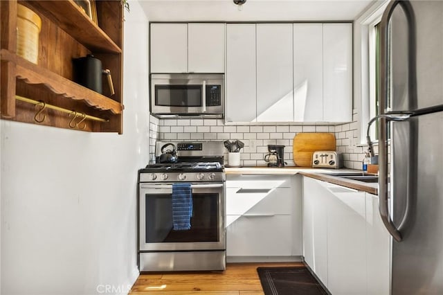 kitchen with white cabinets, backsplash, stainless steel appliances, and light hardwood / wood-style floors