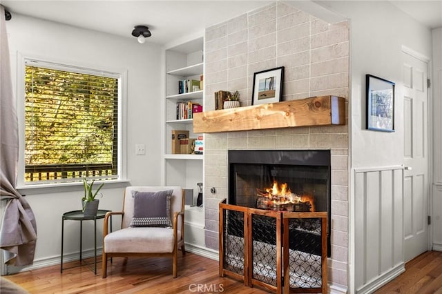 living area with hardwood / wood-style flooring, plenty of natural light, built in features, and a tiled fireplace