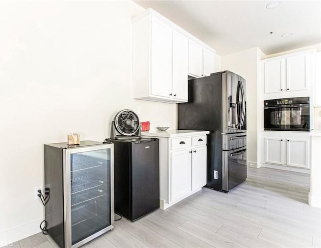 kitchen with beverage cooler, black oven, stainless steel fridge with ice dispenser, and white cabinets