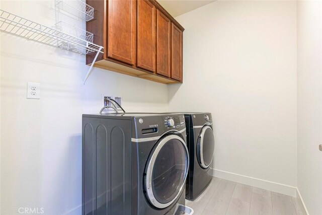 clothes washing area with light wood finished floors, washer and clothes dryer, cabinet space, and baseboards