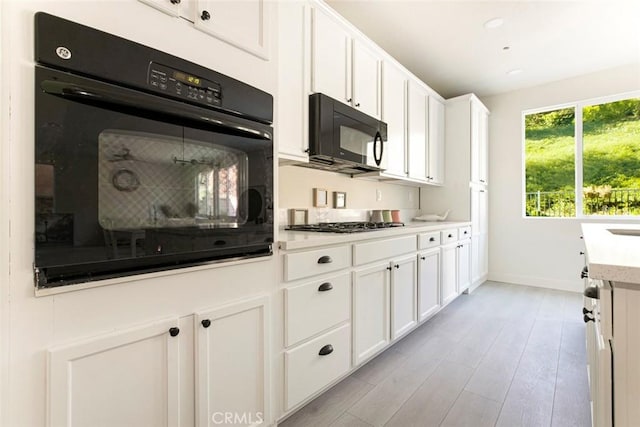 kitchen featuring black appliances, light countertops, light wood-style flooring, and white cabinets