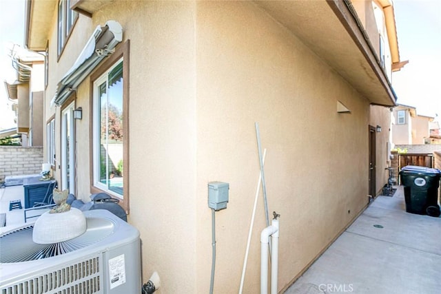 view of side of home with fence, central AC, and stucco siding