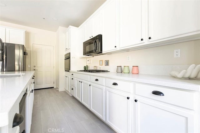 kitchen featuring light wood-style floors, white cabinets, light countertops, and black appliances