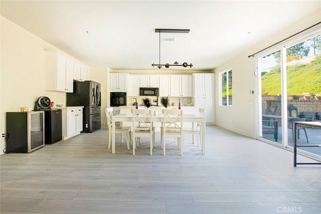 kitchen featuring white cabinetry, light countertops, black appliances, light wood finished floors, and decorative light fixtures