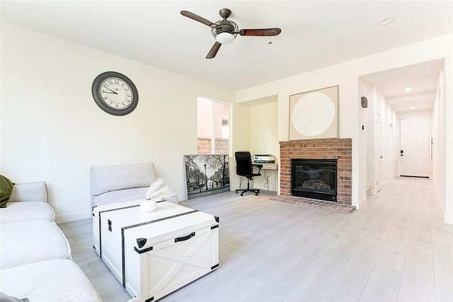 living area with light wood-style floors, ceiling fan, a fireplace, and baseboards