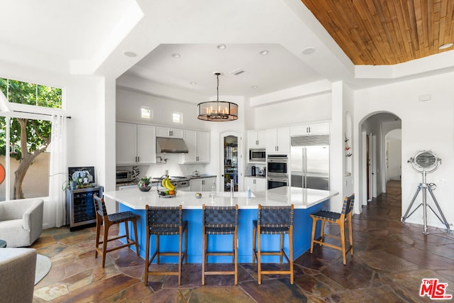 kitchen with hanging light fixtures, a raised ceiling, built in appliances, a breakfast bar, and white cabinets