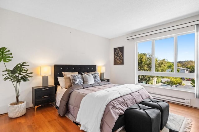 bedroom with a baseboard heating unit and light hardwood / wood-style floors