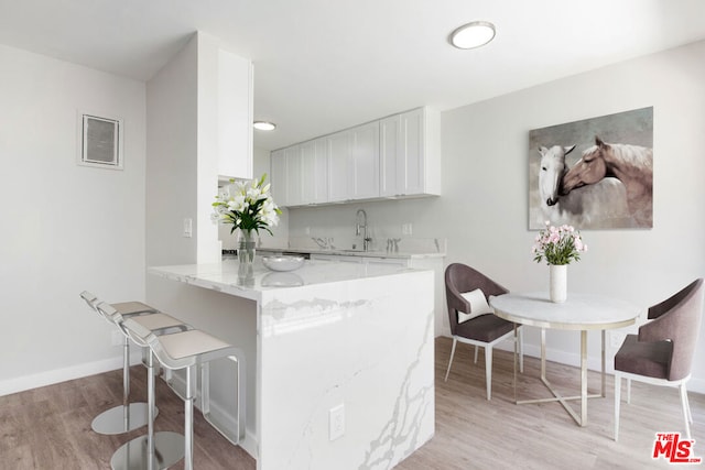 kitchen featuring light stone countertops, white cabinetry, kitchen peninsula, light hardwood / wood-style floors, and a kitchen bar