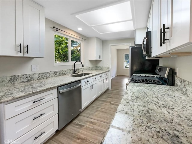 kitchen with light stone counters, stainless steel appliances, sink, light hardwood / wood-style flooring, and white cabinets