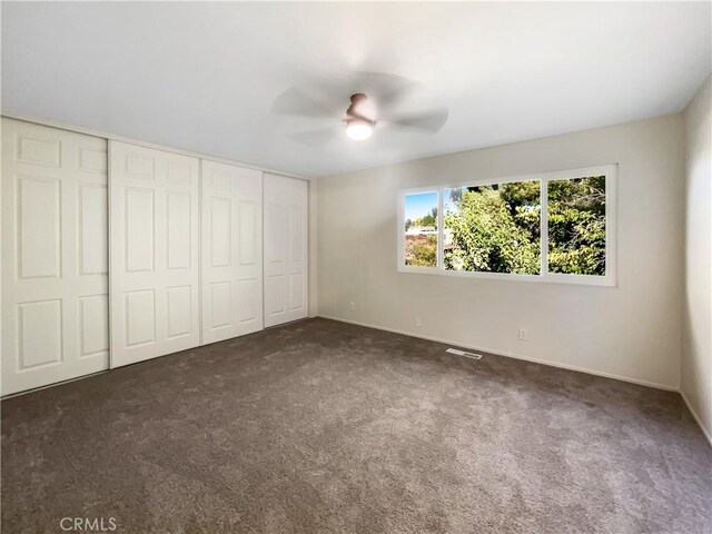 unfurnished bedroom featuring dark colored carpet, a closet, and ceiling fan