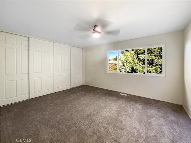 unfurnished bedroom featuring ceiling fan, a closet, and dark colored carpet