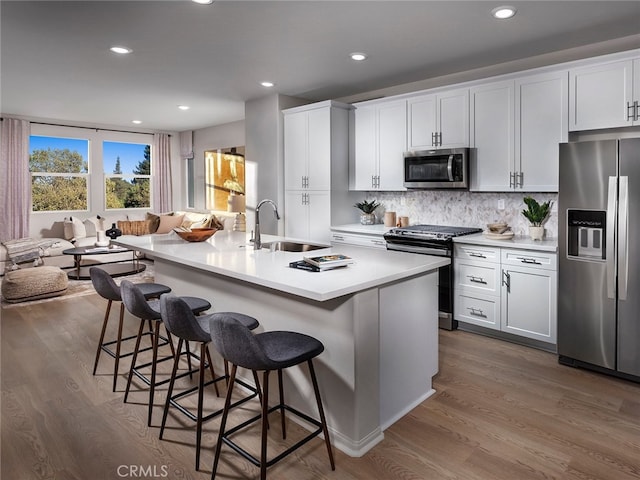 kitchen featuring sink, stainless steel appliances, white cabinetry, and an island with sink