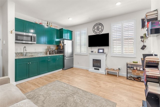 kitchen with appliances with stainless steel finishes, light wood-type flooring, a healthy amount of sunlight, and sink