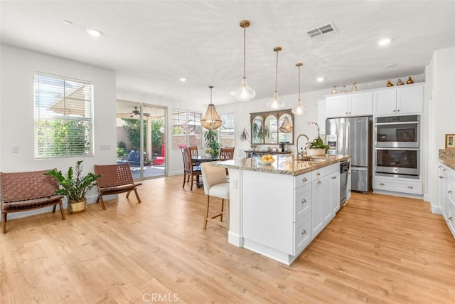 kitchen featuring white cabinets, light stone countertops, and an island with sink