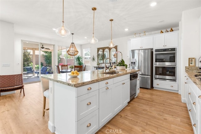 kitchen with white cabinetry, sink, decorative light fixtures, a center island with sink, and appliances with stainless steel finishes